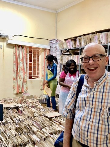 A man stands behind stacks of paper files.