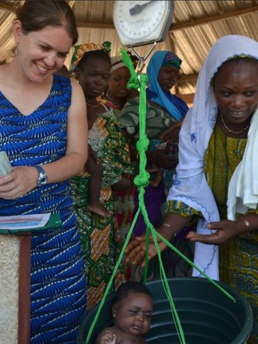 Two women weigh an infant using a bucket