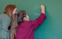 Student and teacher write words on blackboard during English lesson