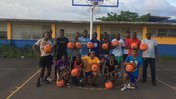 A basketball team of young Jamaican men and women pose with donate basketballs with volunteer Don Holly.