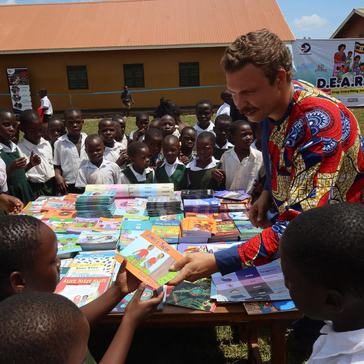 Ben presents a large book donation to the children at the official opening of a school library in Uganda.