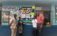 Four Jamaicans stand in front of a school literacy mural
