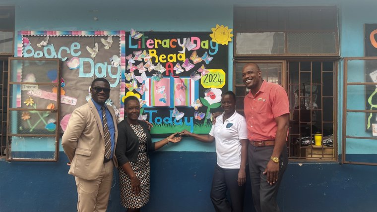 Four Jamaicans stand in front of a school literacy mural
