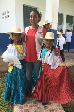 Latinx Volunteer in jeans poses with two young Panamanian girls in traditional dress.