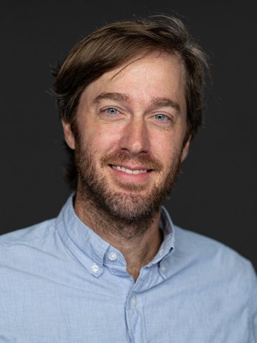 A middle-aged man smiles in a blue buttondown shirt.