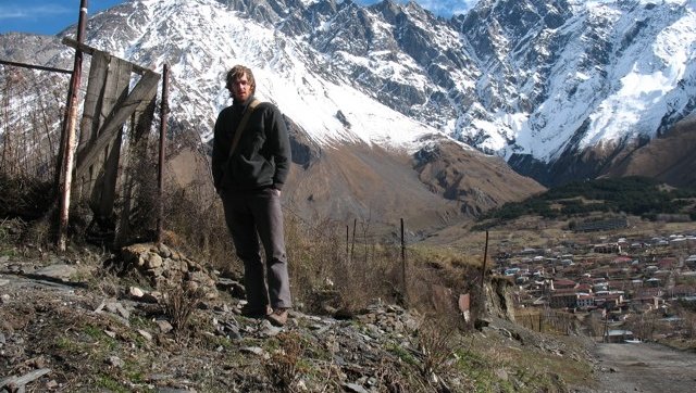A male hiker stands in front of a snow-covered mountain