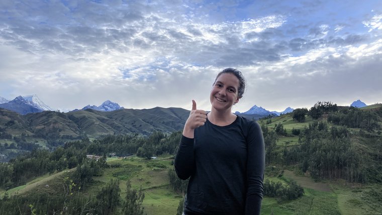 Volunteer standing in front of a mountainous and green landscape in Peru.
