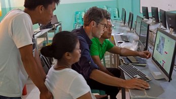 A male Caucasian Peace Corps Volunteer sits in front of a computer, looking intently at a land use map model. 3 of his Filipi