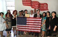 A group of people stand behind an American flag, smiling.