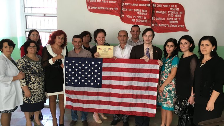 A group of people stand behind an American flag, smiling.