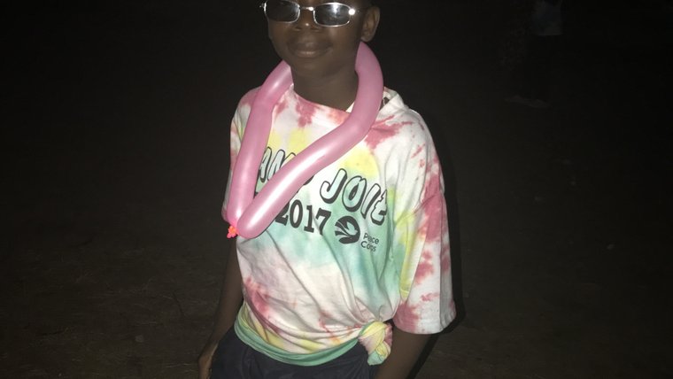 A Child with his camp t-shirt, smiling with a balloon animal around his neck.