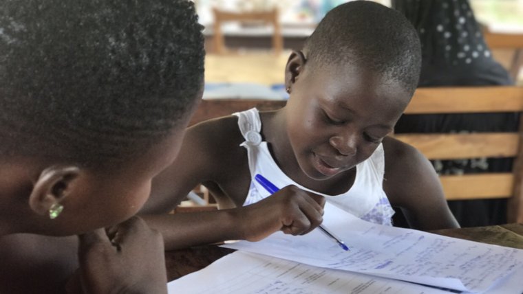Young smiling Togolese girl pointing with a pin at her written action plan in a notebook.