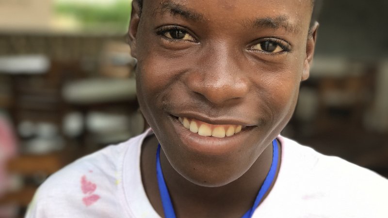 A Togolese boy smiling wearing "Camp Joie" t-shirt.