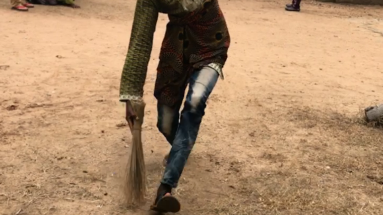 A Togolese girl running with a bucket on her head and a traditional broom in her hand.