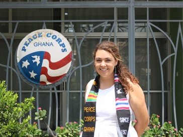 A woman stands in front of a Peace Corps Ghana sign