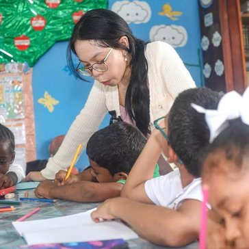 Female leans over students while guiding them through literacy session in the classroom.