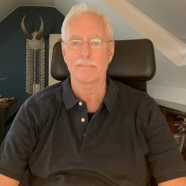 An older white male faces the computer camera in his home office