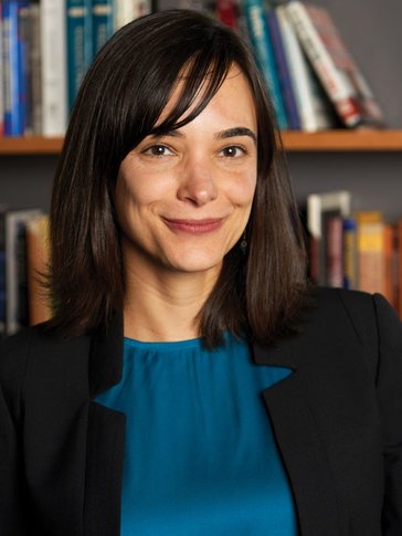 A woman in a blazer smiles in front of a bookcase