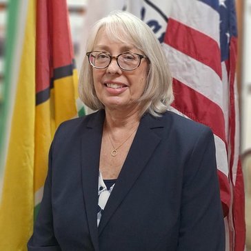 Woman standing in front of flags representing Guyana, the United States and the Peace Corps.