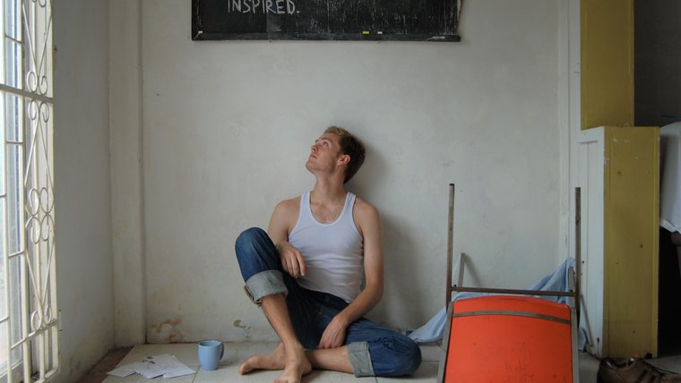 Returned Volunteer Chase sitting under a sign that reads inspired