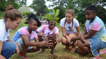 Two women plants seeds in Jamaica with young girls