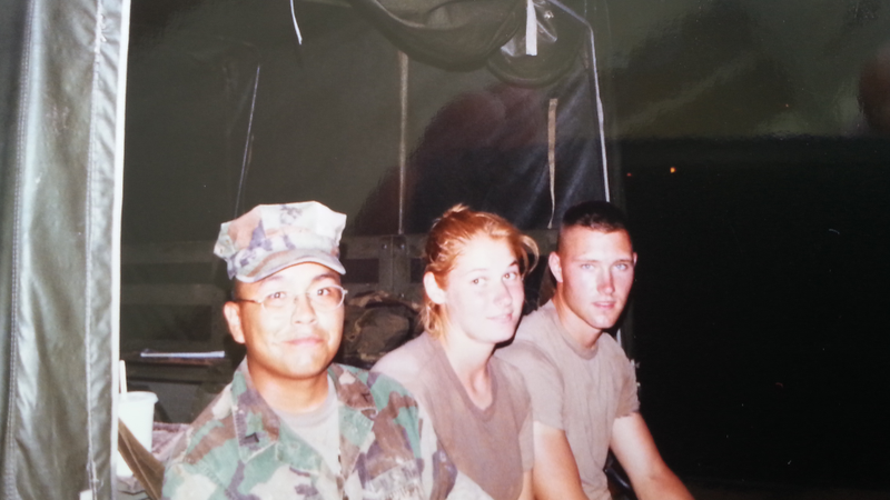 An American female Marine smiles while sitting on the back of a truck with a fellow American and a Thai national in army fati