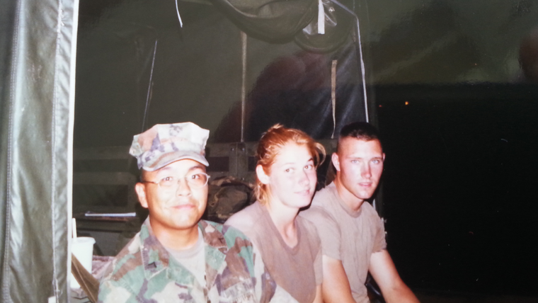 An American female Marine smiles while sitting on the back of a truck with a fellow American and a Thai national in army fati