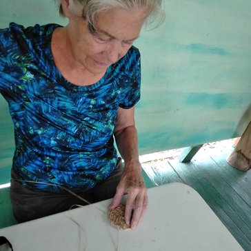 A woman weaves a drink coaster out of banana fibers.