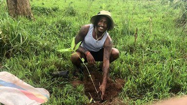 A Volunteer poses behind his newly planted bamboo seedling
