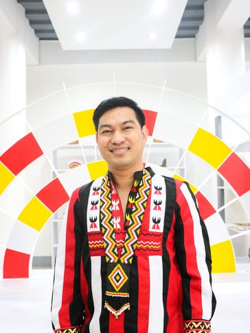 A Filipino man stands smiling in a red, white, and yellow striped top