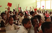 Children in a classroom raise their hands during an HIV education activity.