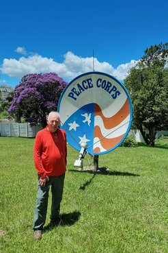 An older white male stands in front of a Peace Corps sign outside