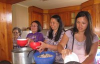 Four Asian American women stand side by side in a kitchen. They are cooking together.