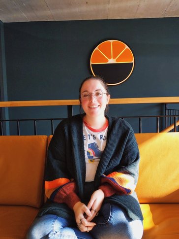 A woman sits smiling in a colorful cardigan