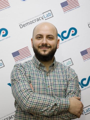 A bald man stands with his arms crossed across his chest