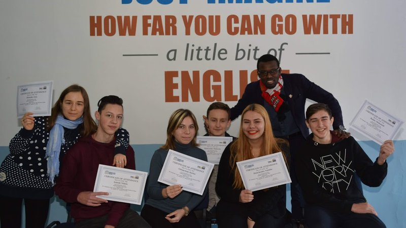 Volunteer Fabenson Frisch poses with six locals. They're smiling and holding certificates of English Camp completion.