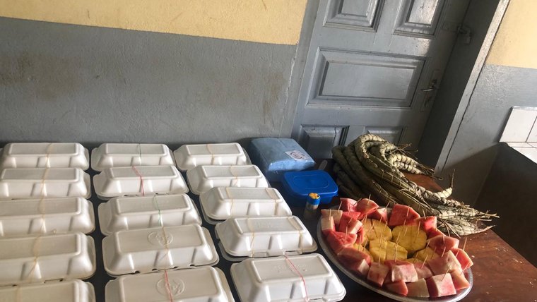 Take away containers and a plate of fruit are set on a wooden table.