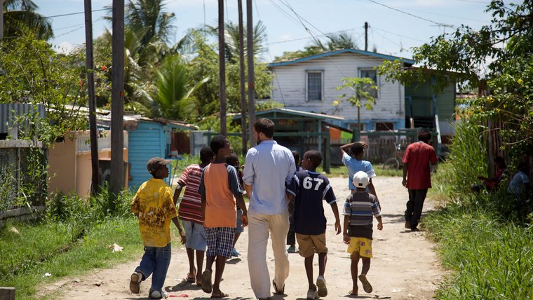 a peace corps volunteer walks down a dirt road in Guyana with local boys