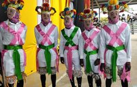 Five masked men wear pink and green sashes over an all-white outfit.