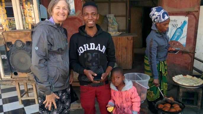 A white woman stands with her Tanzanian friend and a child, smiling.