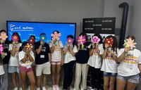 Twelve young students hold handmade paper flowers in front of their faces