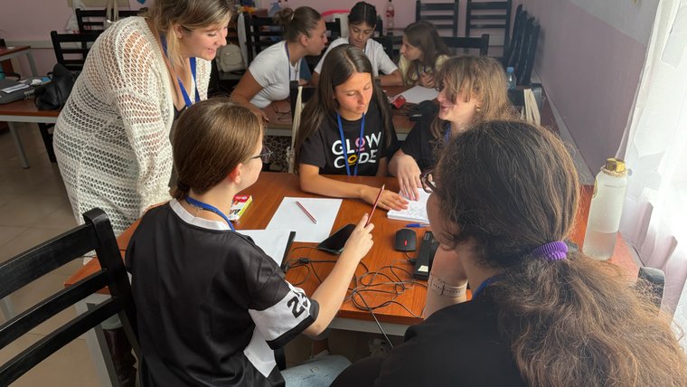 A young female teacher helps a group of four girls with classwork