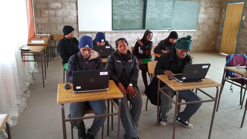 Seven African students work at computers in a classroom in Lesotho