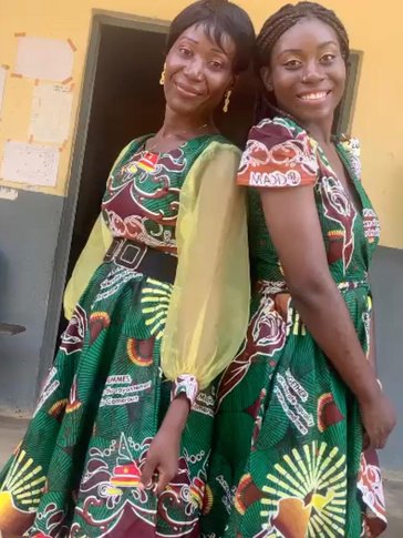 Two smiling black female persons pose for a photo, wearing green gowns made out of African print.