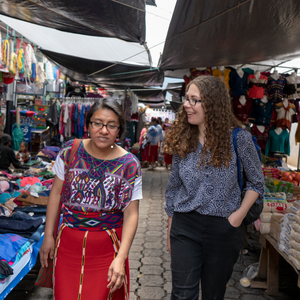 A female Peace Corps Volunteer walks with a Guatemalan counterpart through a busy open air market.
