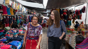 A female Peace Corps Volunteer walks with a Guatemalan counterpart through a busy open air market.