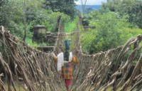 A woman crosses over a river on a rope bridge.