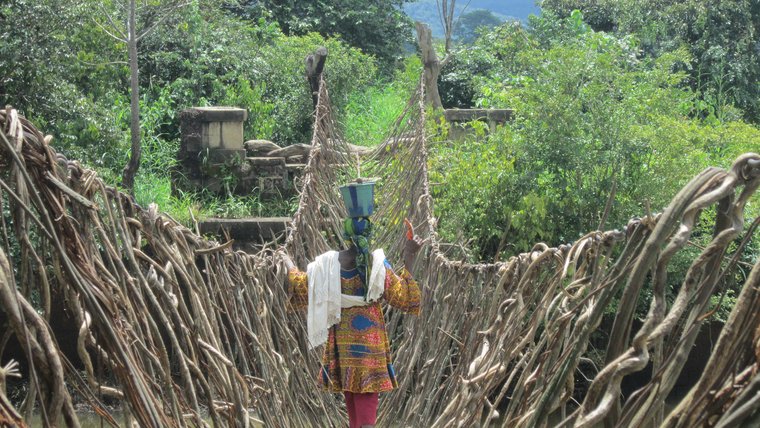 A woman crosses over a river on a rope bridge.