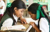 Two girls in school uniforms read a book together.
