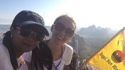 Volunteer Lainey Heyl and fellow teacher Daw Hnin Nu Nwe stand next to a flag, with a view of mountains behind them.